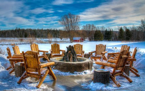 Wooden chairs around a large outdoor firepit during winter. 