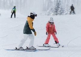 A ski instructor and child on skis on a snowy hill. 