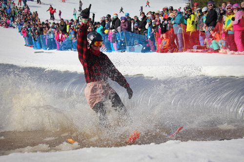 A man on skis gliding over a pool of water surrounded by snow and spectators. 