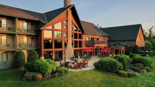 exterior of the lodge with a fire pit out front and tables with umbrellas out front.