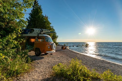 A man and woman sitting beside a vintage van on the shore of Lake Michigan.