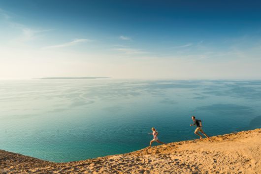 A boy and girl running along a sand dune over Lake Michigan.