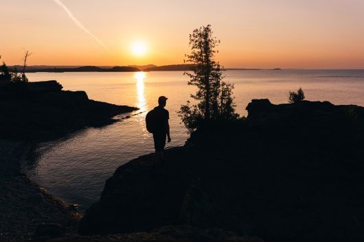 A hiker standing on a rocky shore at sunset. 