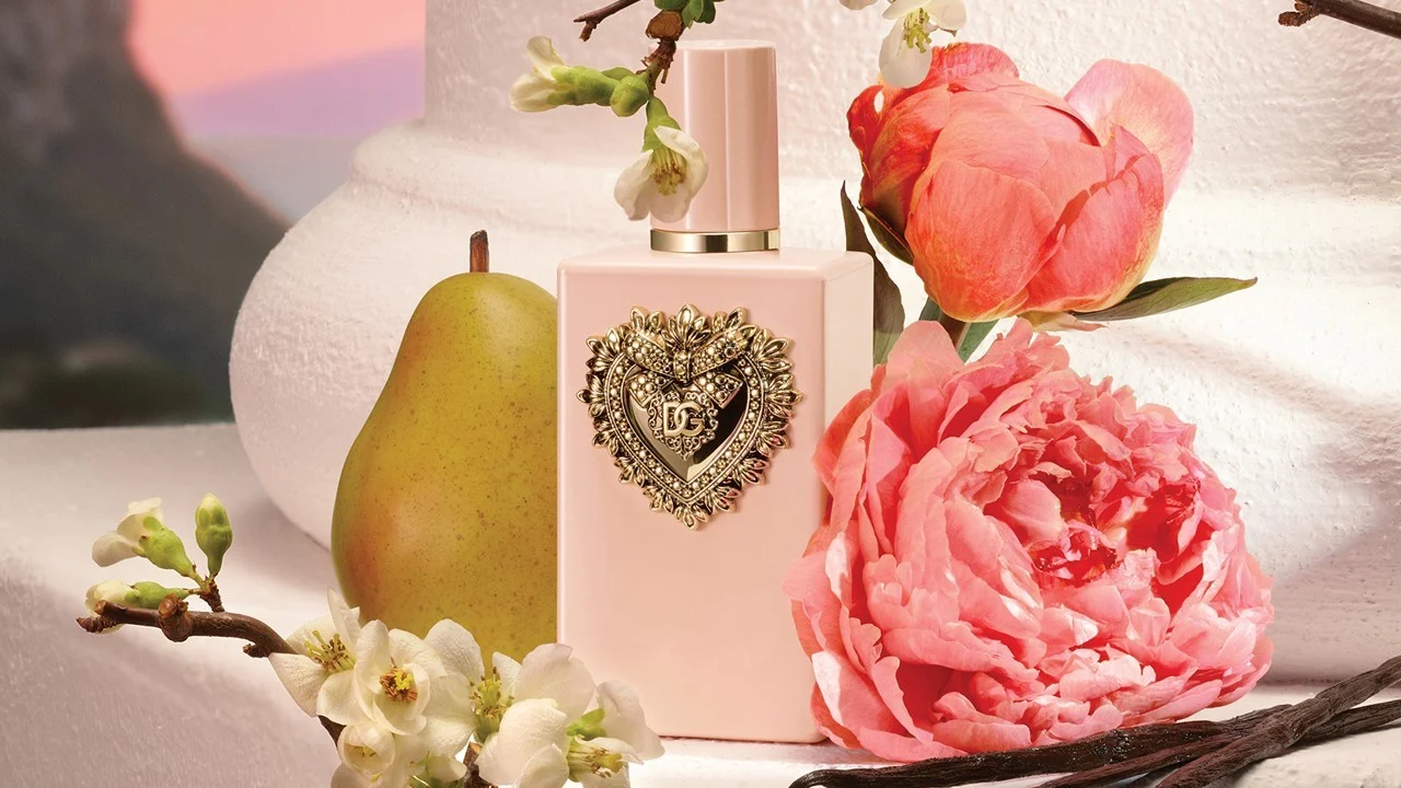 a pink perfume bottle flanked by a rose, some bears, and some little white flowers