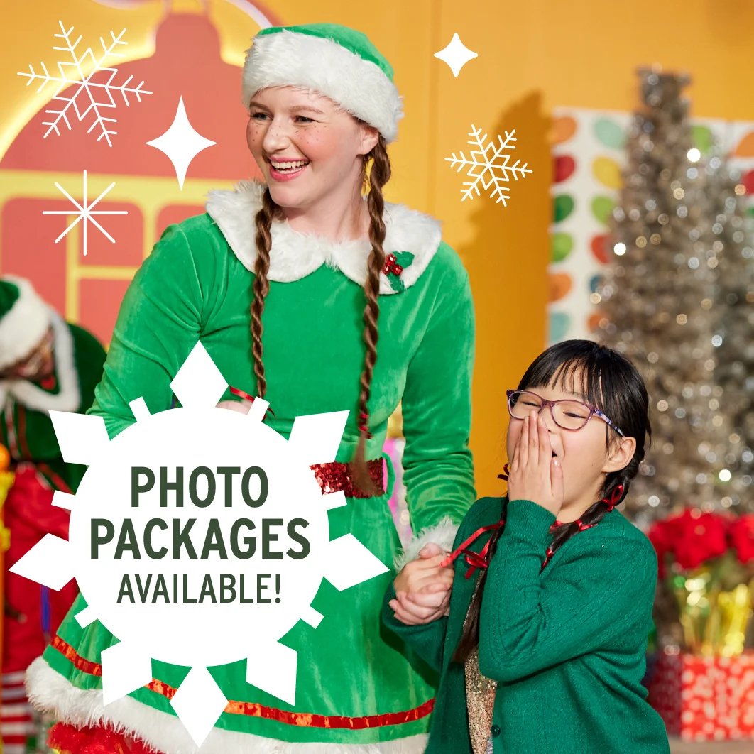 an elf in a green dress holding a kid's hand in front of a silver tree and presents