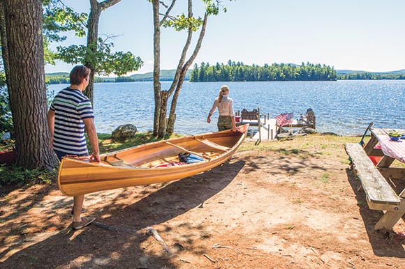 a man and woman carrying a canoe to the lake