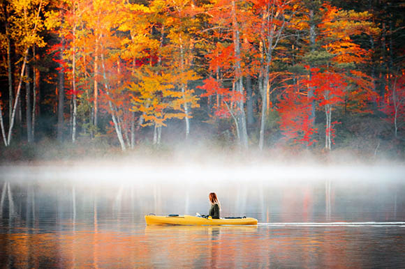 a woman in a kayak with foliage behind her