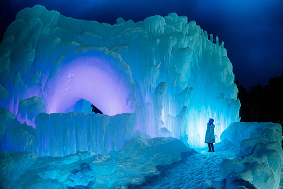 a person standing next to a lit up ice castle at night