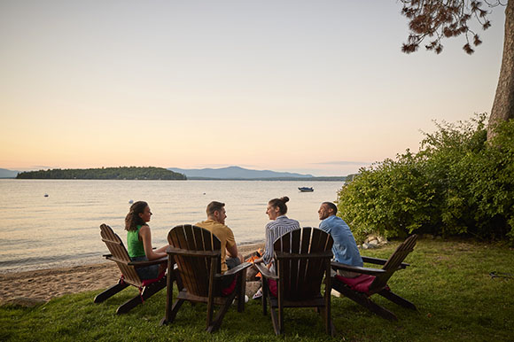 a group of friends sitting in chairs looking out at a lake