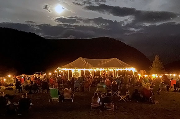 musicians under a tent with lights in the mountains