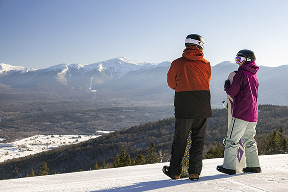 two snowboarders looking at a view of snow covered Mt. Washington