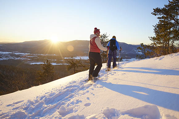 a man and woman snowsheing at sunset with a vista in background