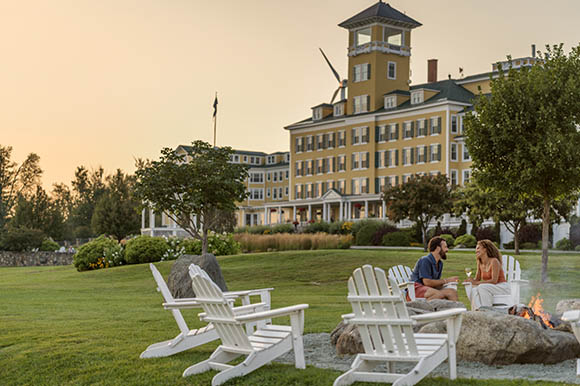 a man and woman sitting outside a large yellow hotel at sunset