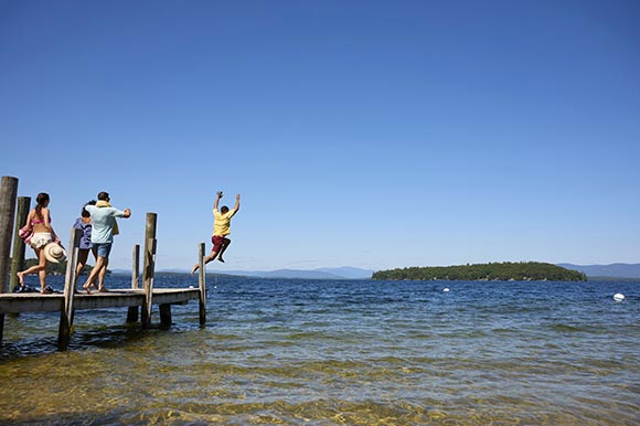 a man leaping from a dock into the water, with friends behind him