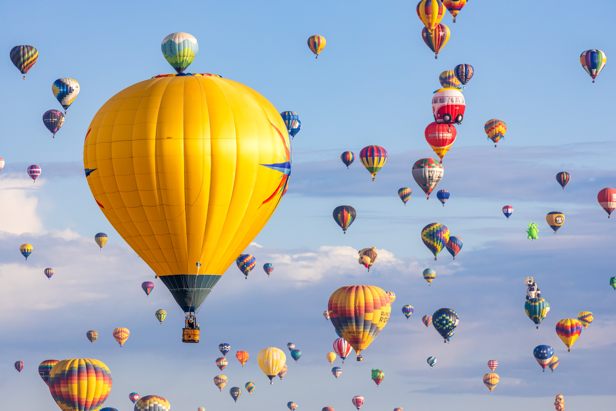 a large group of multicolored hot air balloons float through a blue sky with fluffy white clouds in the distance