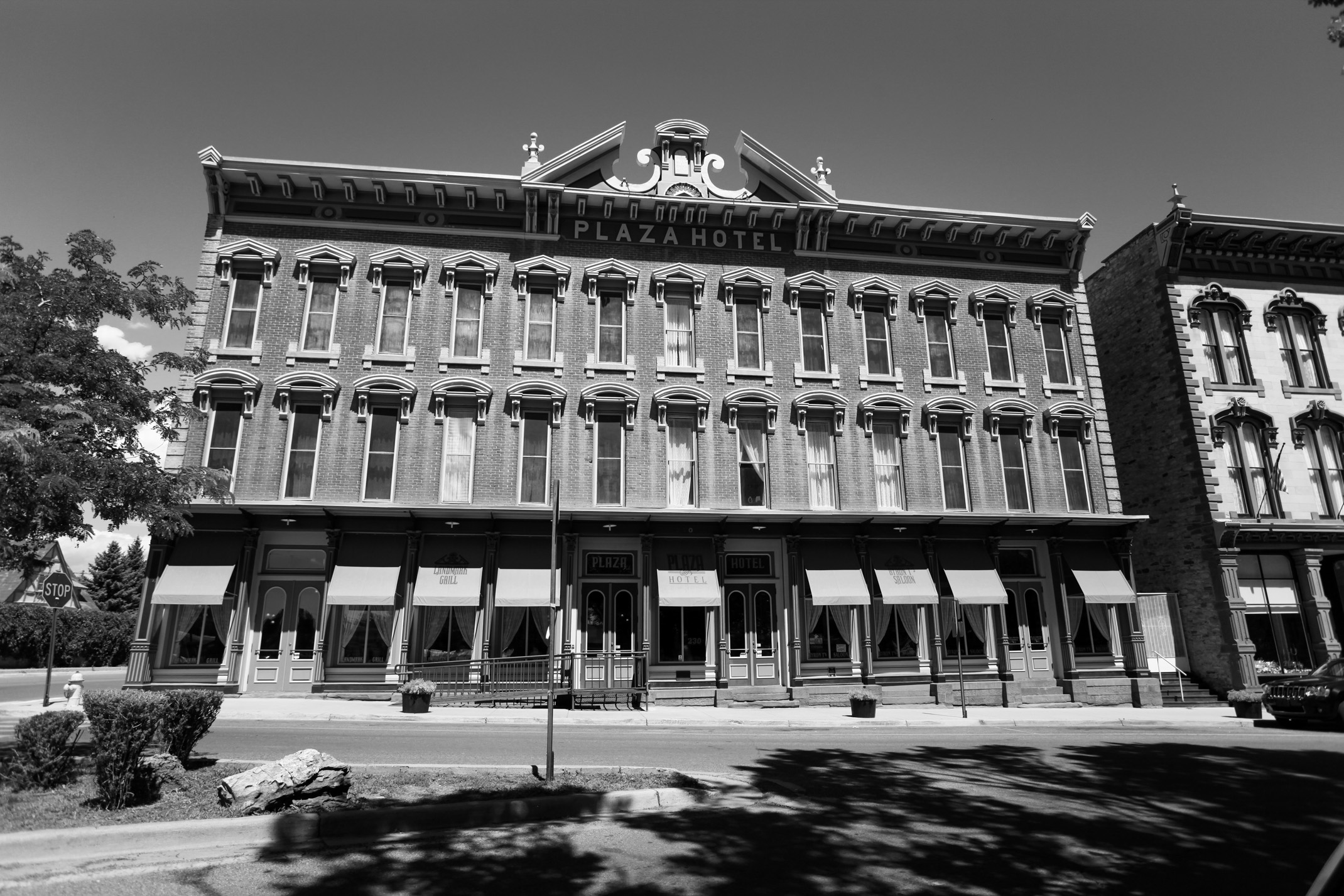 a black and white image of a large brick building on a quiet street with a large sign saying Plaza Hotel