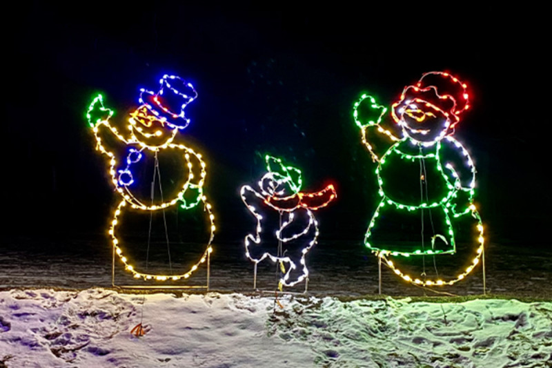 Colorful light displays of three snowmen of varying sizes, decorated with vibrant lights, are set against a nighttime background with a snowy foreground.