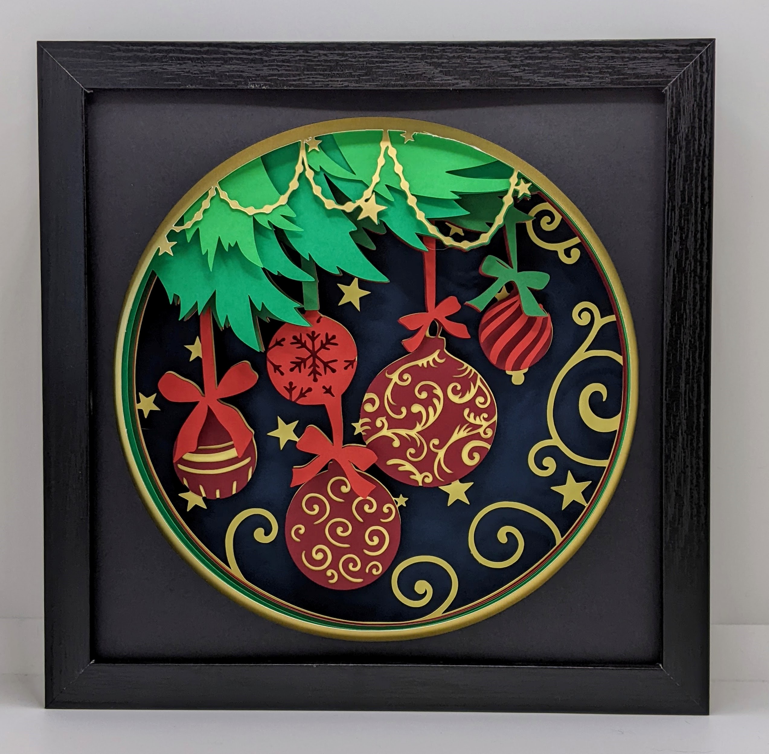 Framed artwork featuring a festive Christmas theme with ornate ornaments, stars, and pine branches against a dark blue background.