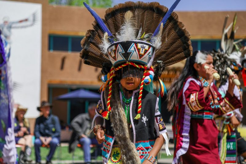 A participant in an elaborate feathered headdress and traditional regalia performs at a Native American cultural event.