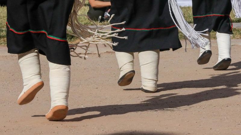 Traditional Puebloan dancers performing in moccasins and ceremonial attire with fringe details, during a cultural performance.