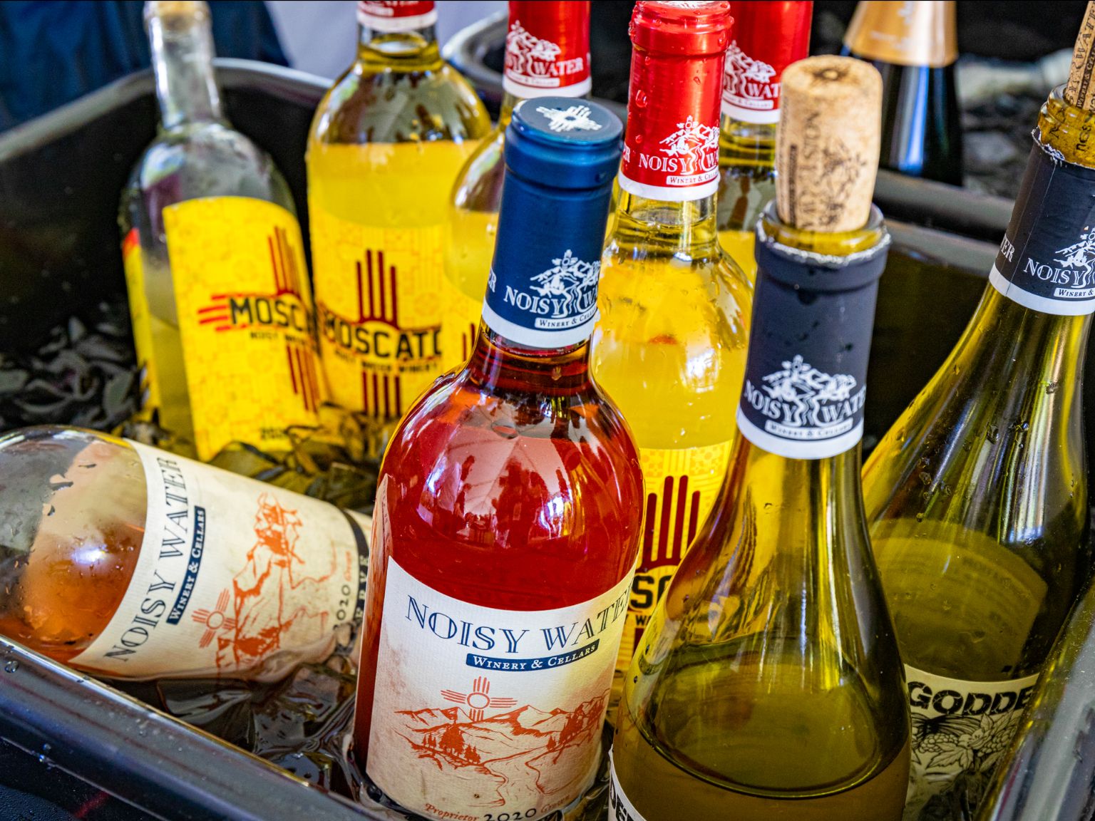 various colorful bottles of wine labeled "Noisy Water Winery" sit in an ice bath