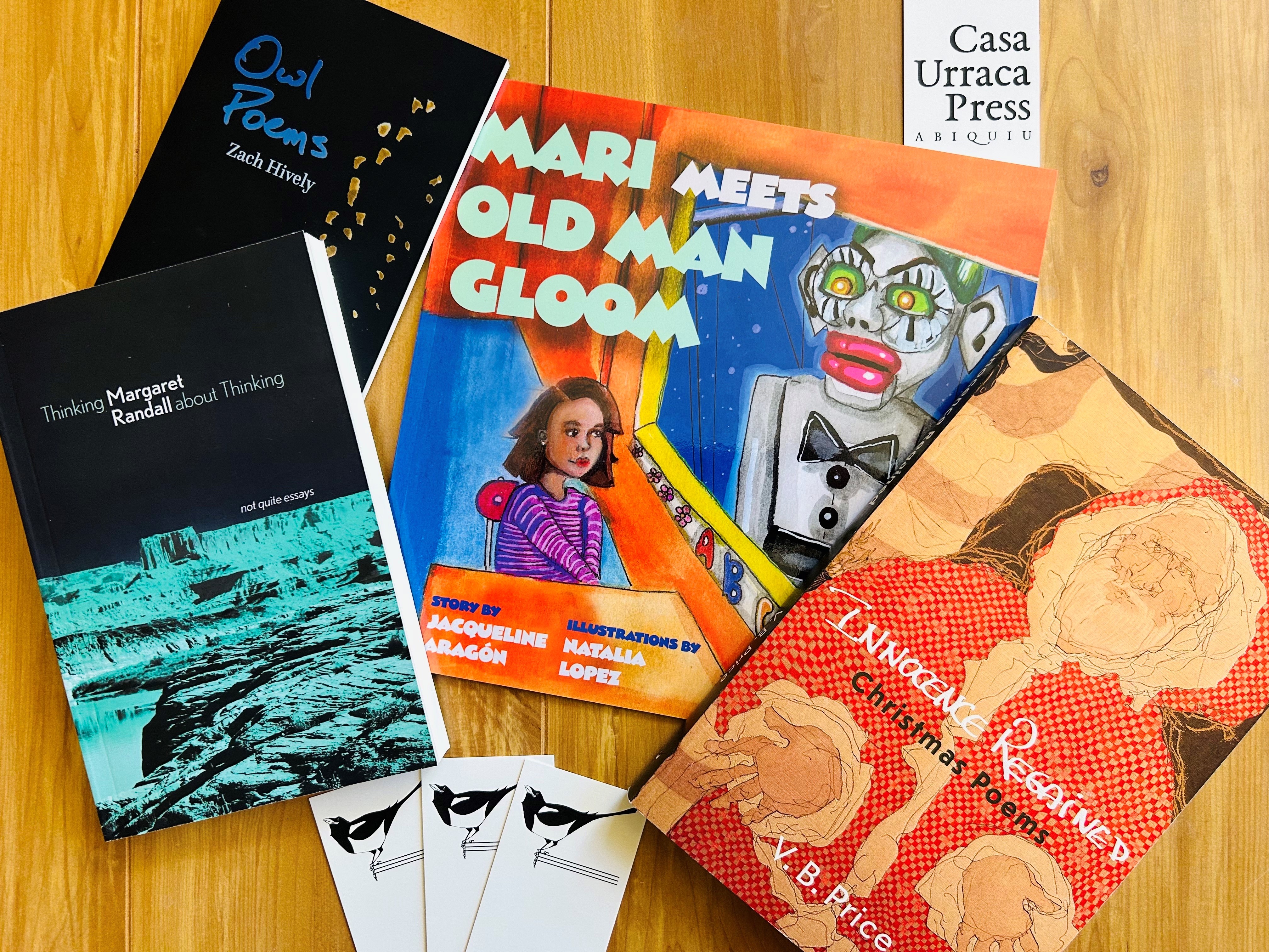 A selection of books and bookmarks on a wooden table, featuring titles like "Mari Meets Old Man Gloom," "Owl Poems," and "Thinking Margaret: Random Thinking." Each book has a distinct cover design, ranging from illustrated characters to abstract patterns.