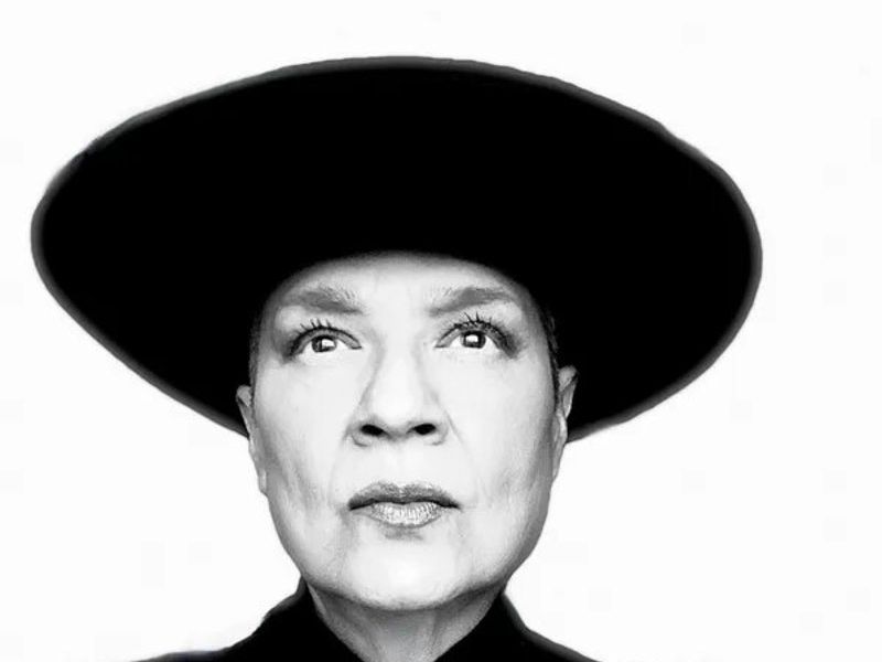 A black and white Portrait of musician Nacha Mendez wearing a large black hat and a black top with a circular white pendant.
