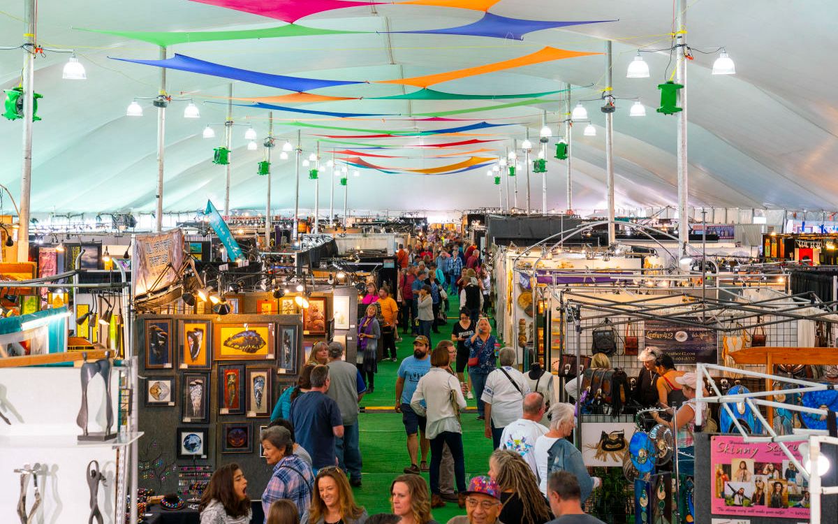 Interior of a bustling fair under a large tent adorned with colorful banners.