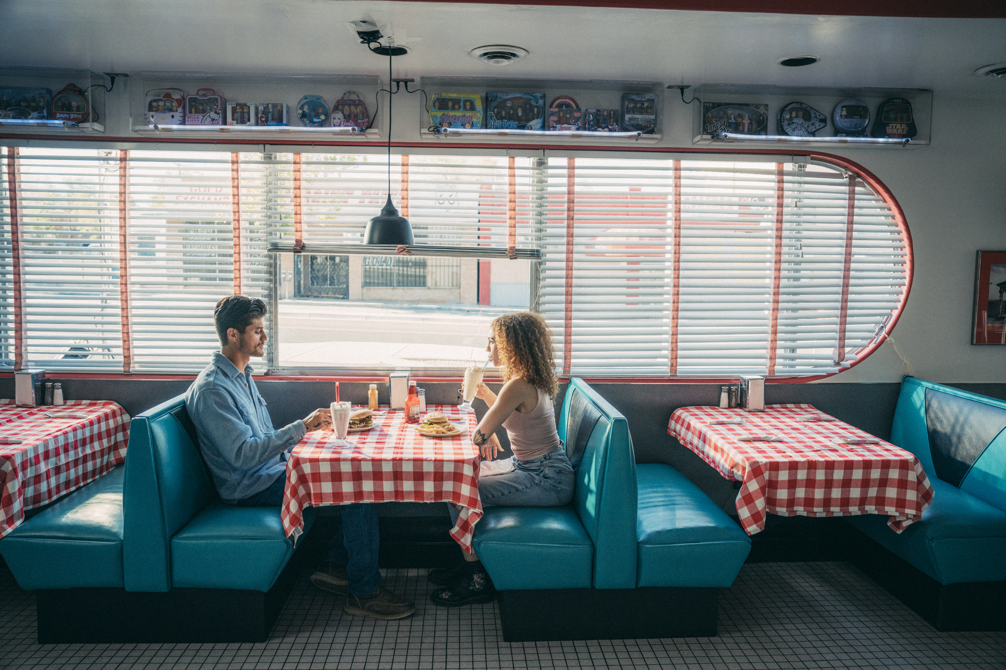 Two people dining across from each other in a booth at a retro-styled diner with sunlight streaming through the windows.