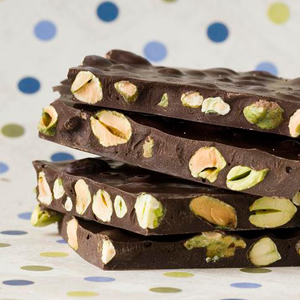 chocolate bars stacked on top of each other, cross sectioned to show pistachios inside, with a colorful dotted background