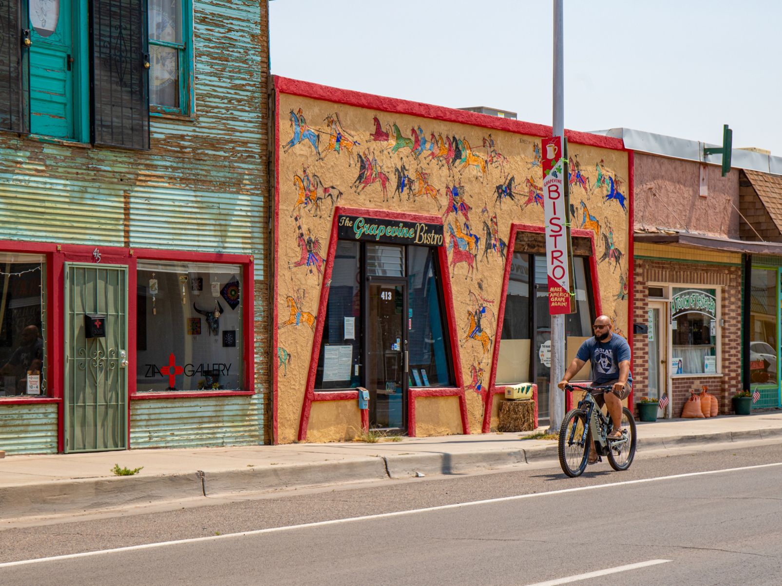 A person riding a bicycle past colorful storefronts on a small-town street.