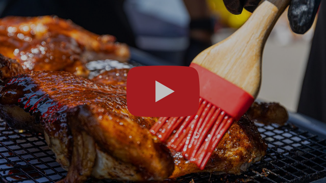 A person brushes sauce onto a piece of meat on a grill
