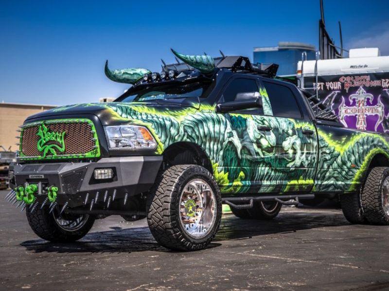 A customized Dodge Ram truck with a vivid green and black dragon-themed paint job, featuring large decorative horns mounted on the roof and specialized green wheel rims.