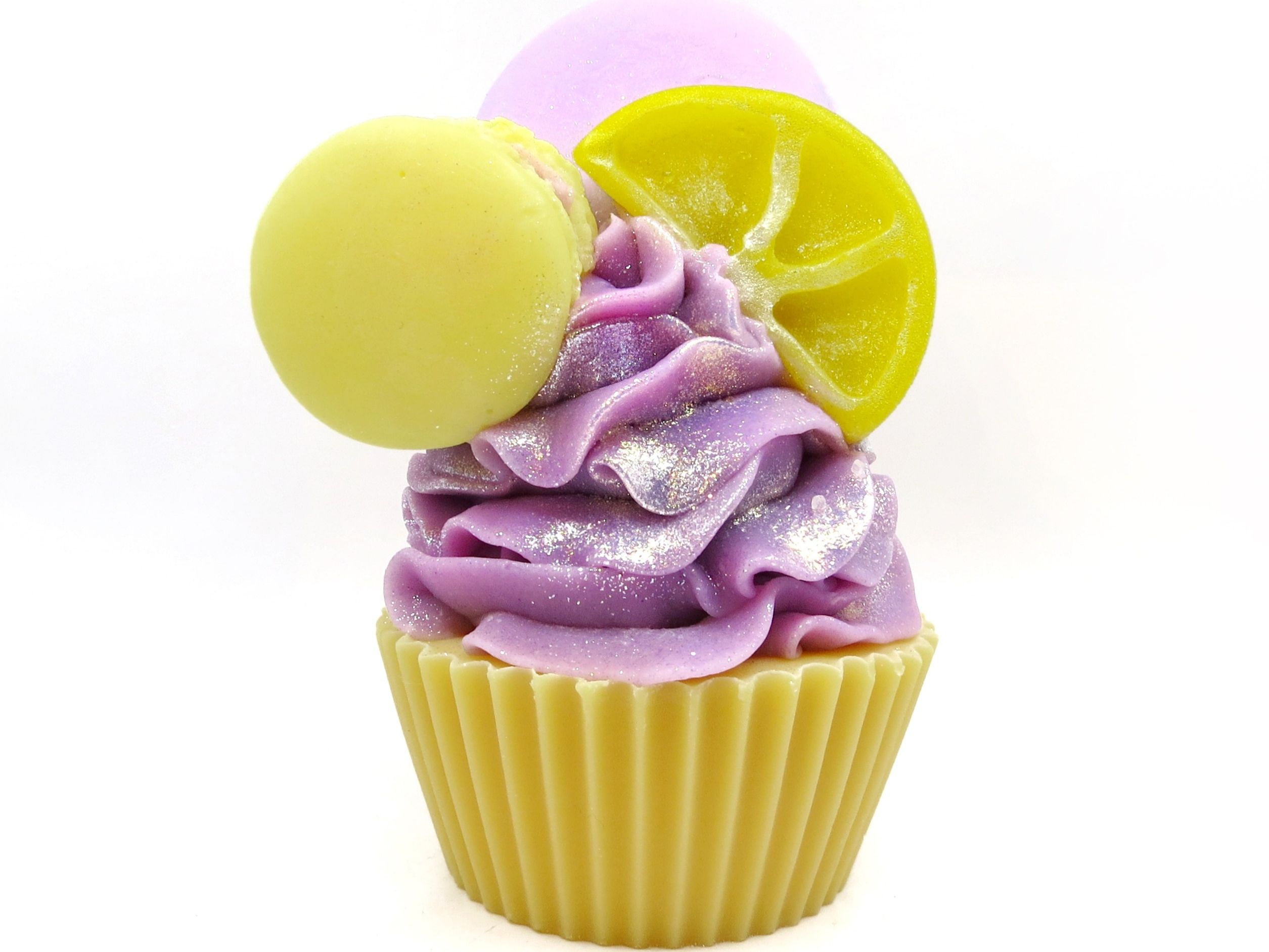 A vibrant cupcake shaped bath bomb with purple frosting, adorned with a yellow and a lavender macaron on top, displayed against a white background.