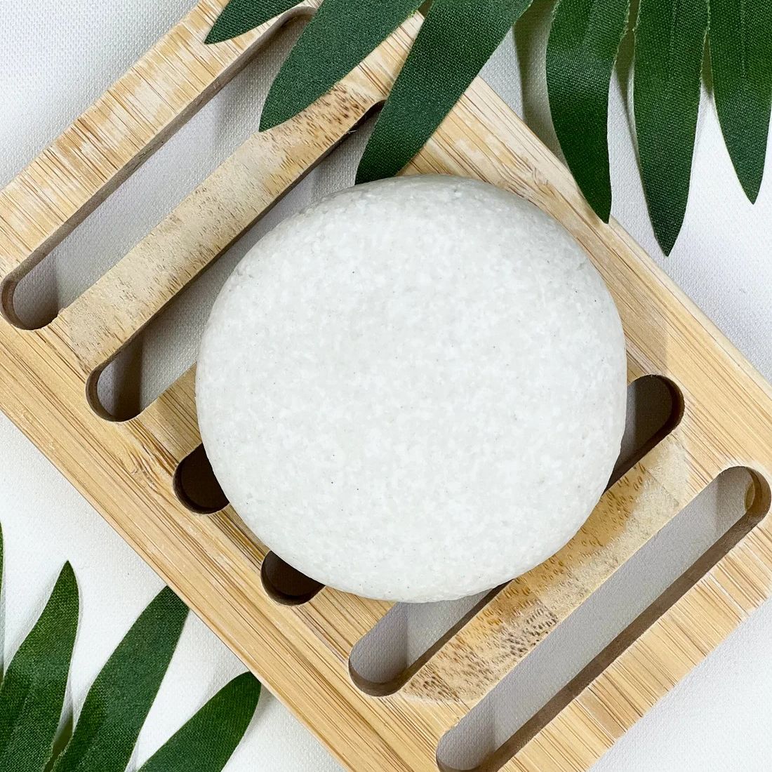 A round white candle placed on a bamboo holder surrounded by green palm leaves.