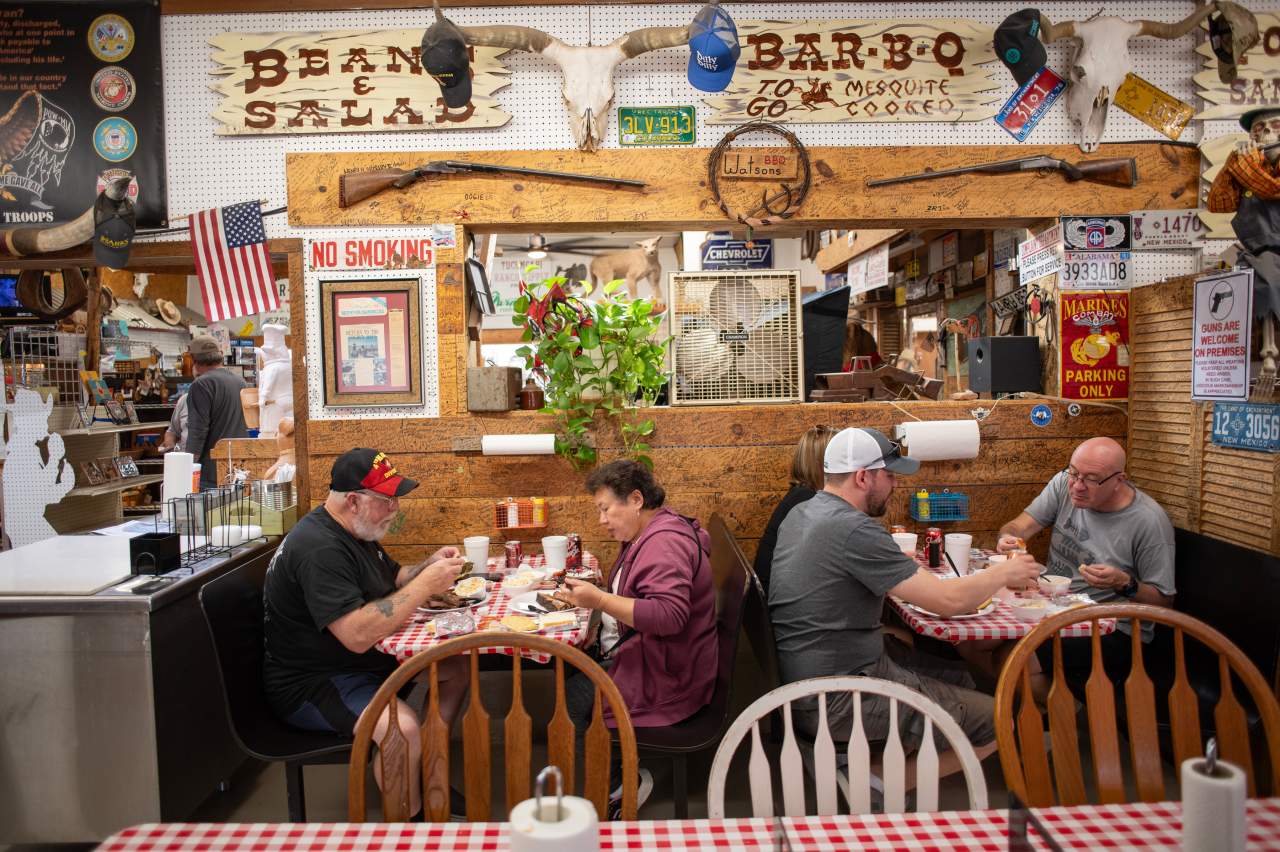 Four people dining at a table in a rustic-themed restaurant with eclectic decor, including signs, flags, and antlers.