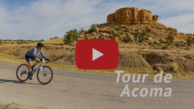 A person riding a road bike on a weathered road with a plateau in the background rising out of the rugged landscape