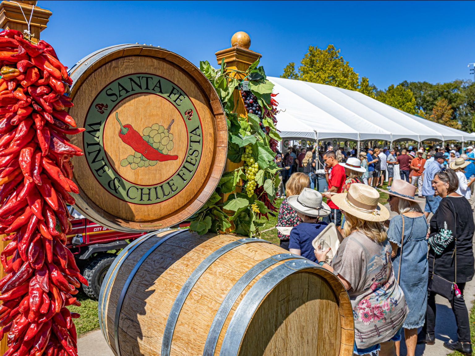 Santa Fe Wine & Chile Fiesta with people gathered under tents, featuring barrels and a decorative chili pepper garland in the foreground.