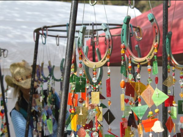 A variety of colorful handmade jewelry and glass ornaments displayed at an outdoor market stall, with a person browsing in the background.