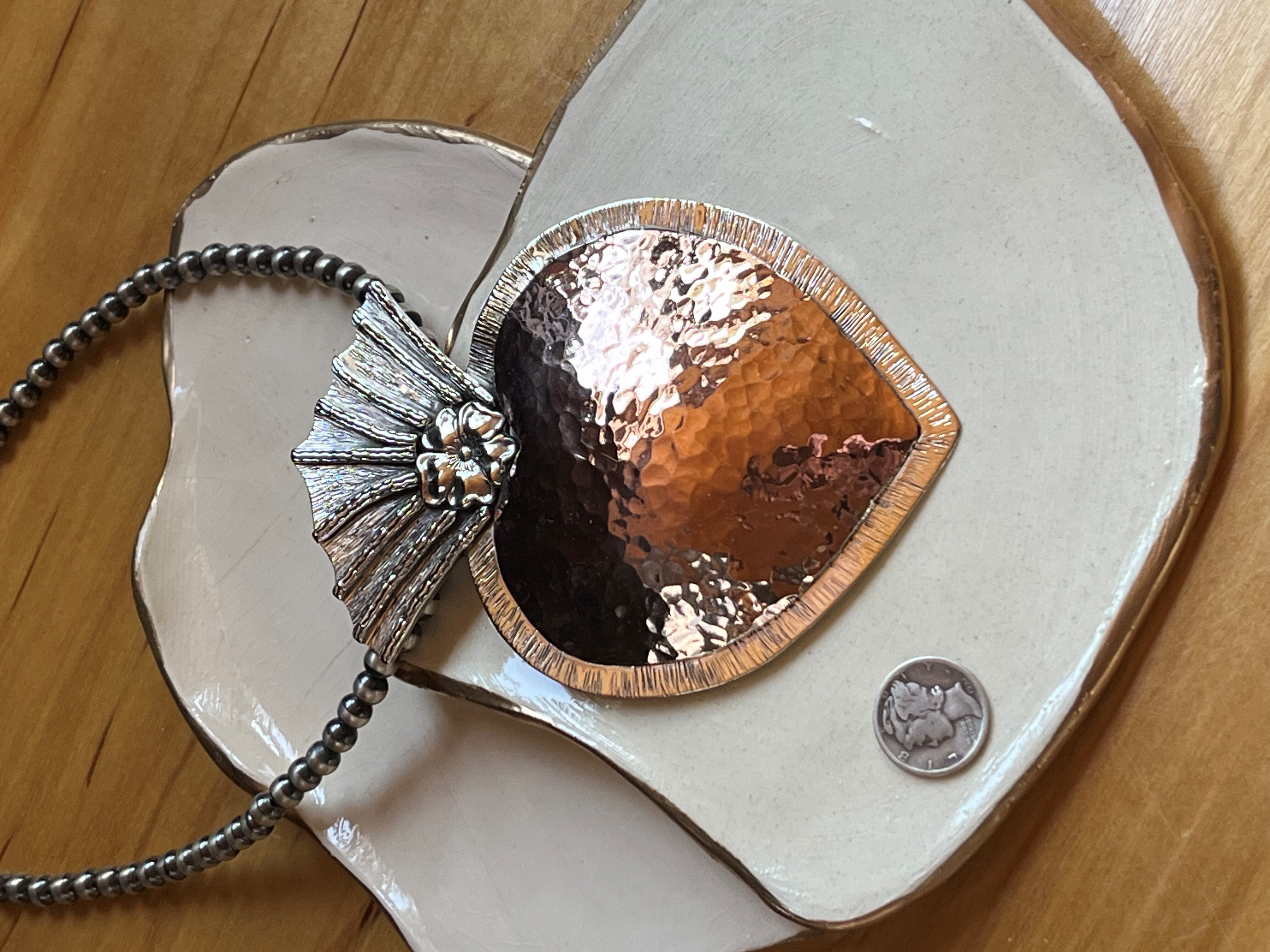 A silver heart-shaped necklace, lying on a ceramic plate on top of awooden surface.