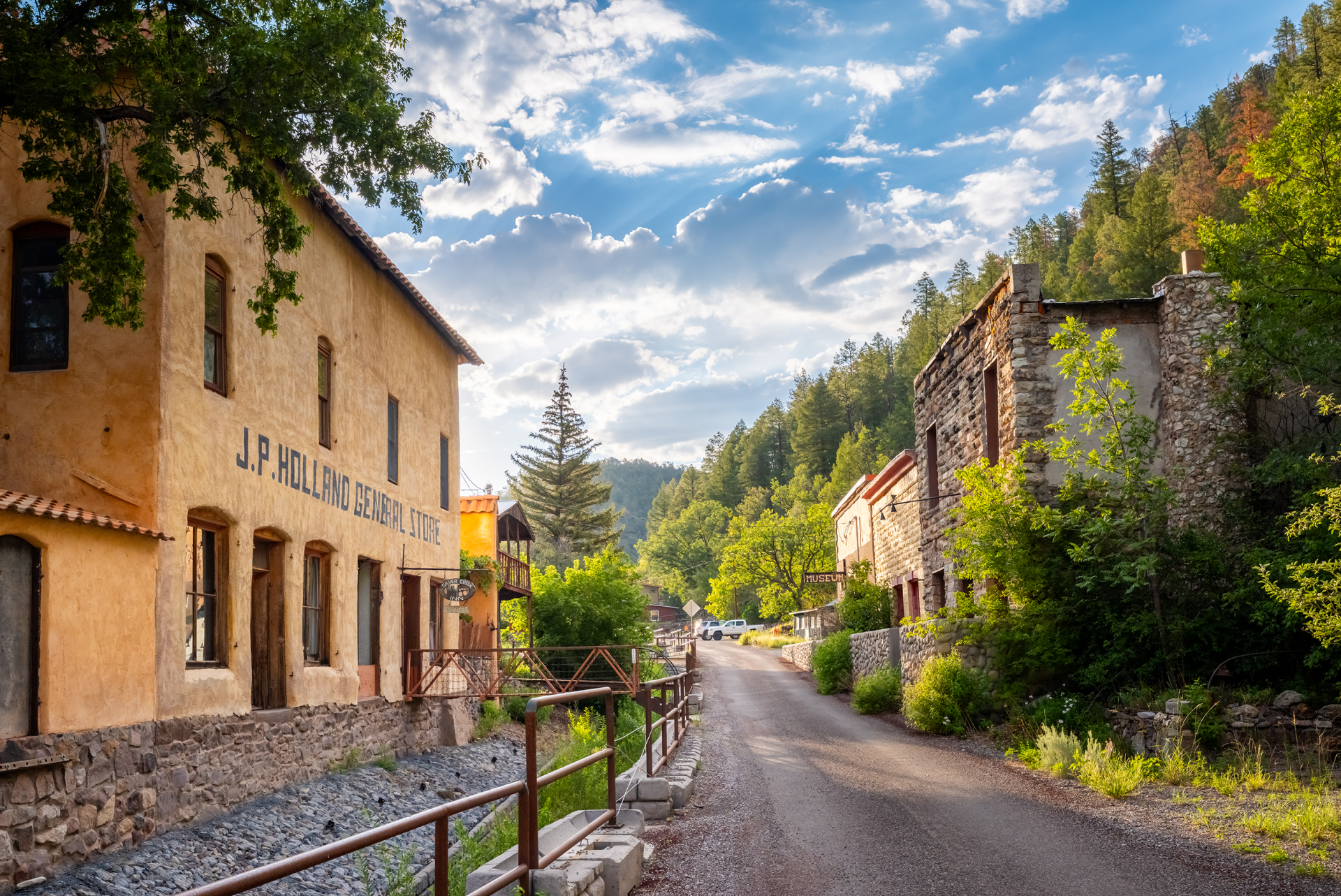 View of a rustic street in Mogollón with old buildings on either side, surrounded by lush trees under a clear sky.
