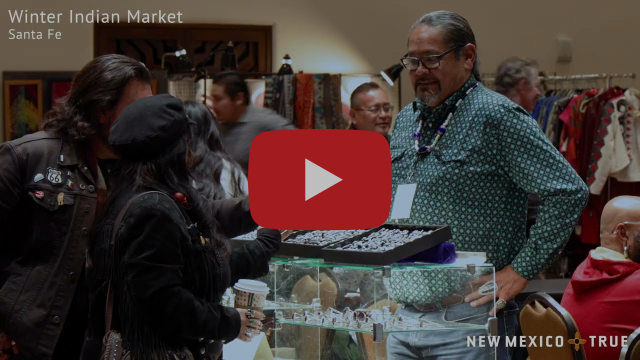 A person stands in front of a booth filled with jewelery at an indoor market.