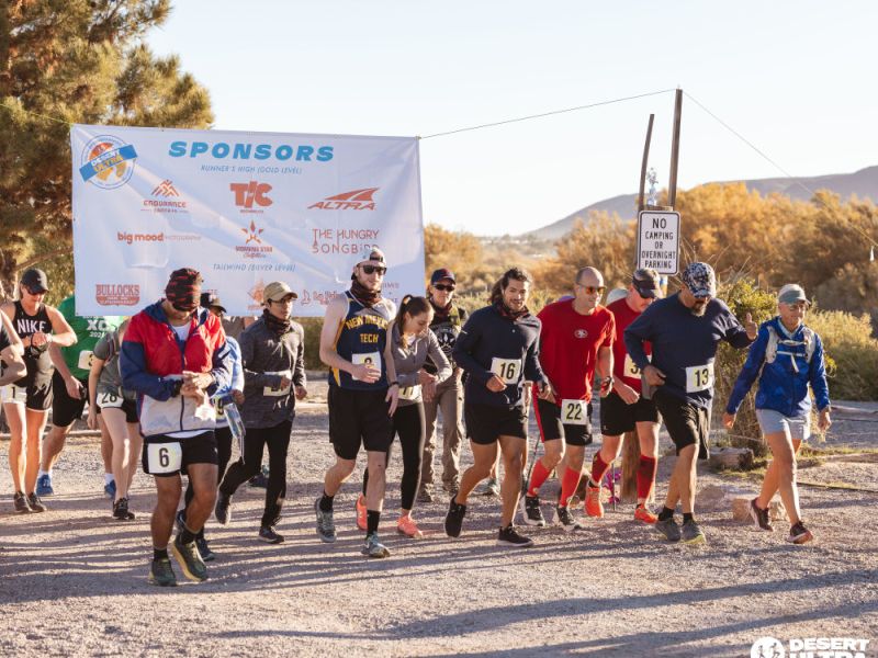 Group of participants starting a race at the Desert Ultra event, with banners behind the runners at a starting line.