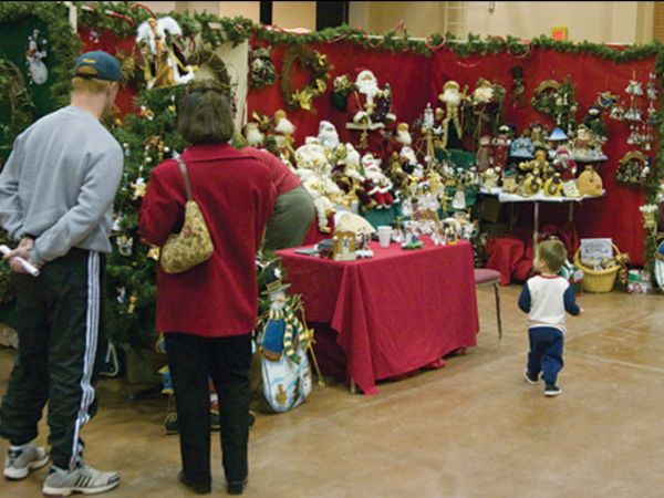 Two adults and a child browsing a Christmas market stall decorated with garlands and filled with festive ornaments and toys.