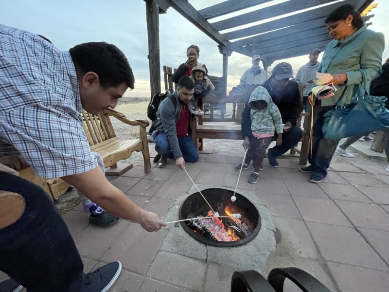 Group of people of various ages enjoying roasting marshmallows over a campfire outdoors at dusk.