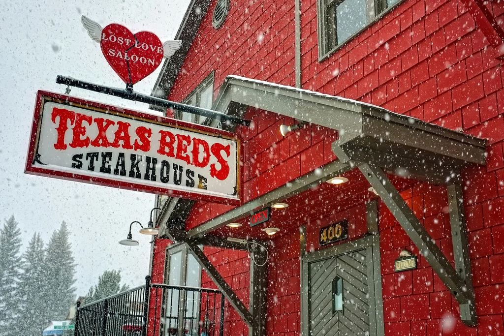 Signs for "Texas Reds Steakhouse" and "Lost Love Salon" on the side of a bright red building during a snowstorm.