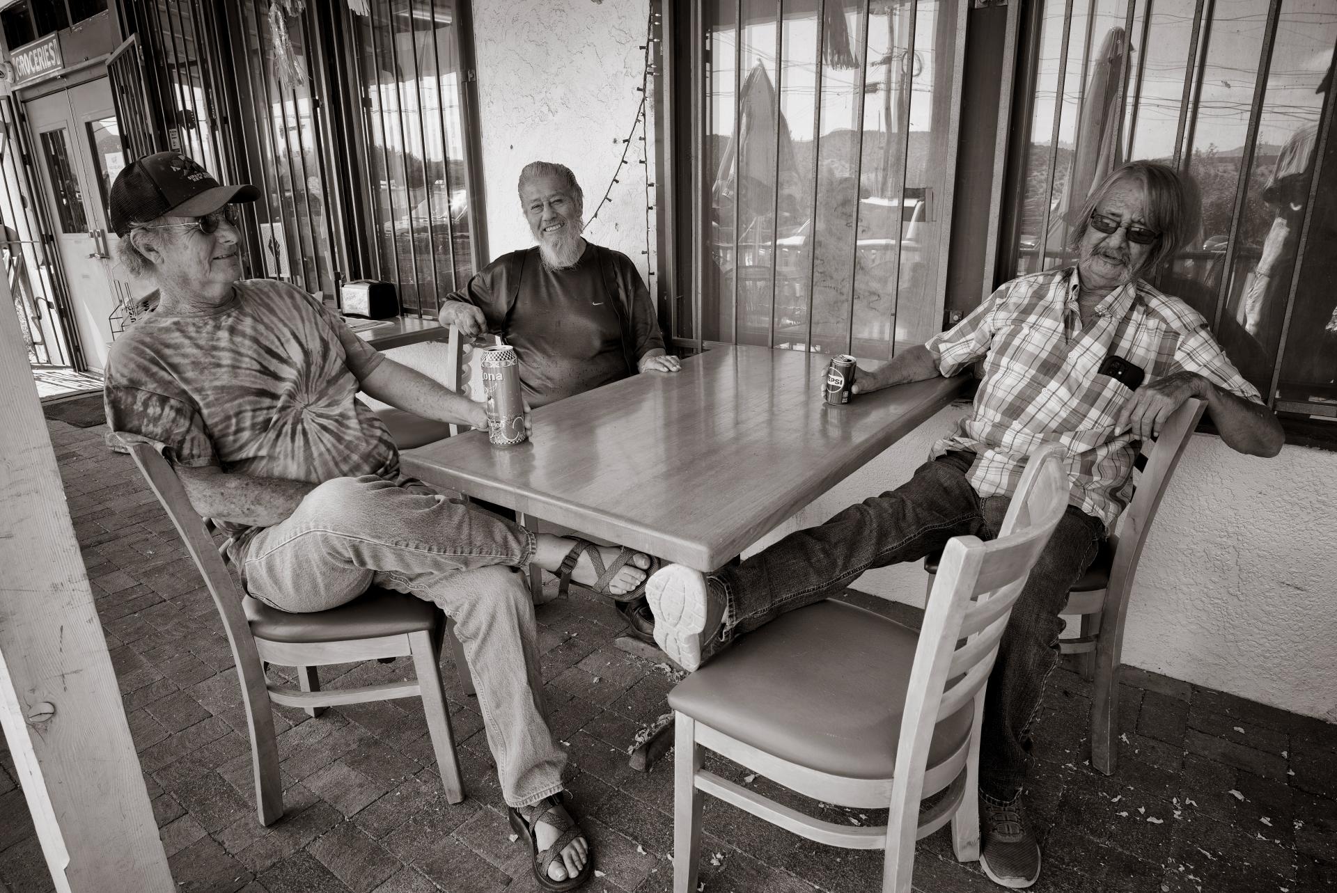 Three individuals lounging and enjoying drinks at a table outside a café.