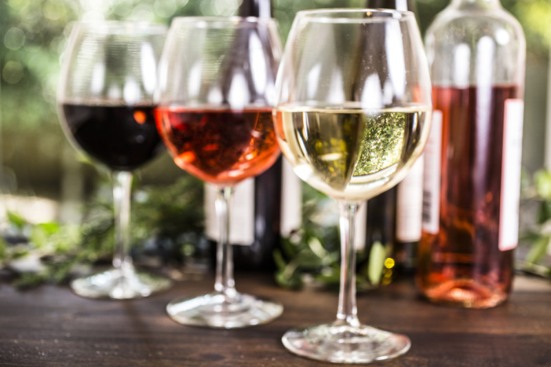 A variety of wine glasses, including red, rose, and white wine, set on a table with a blurred green background.