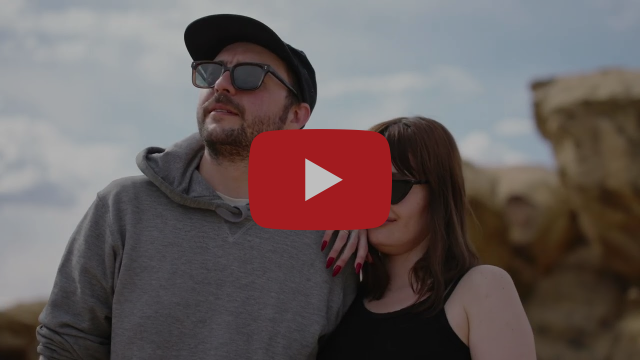 Two people wearing sunglasses stand in front of rocky bluffs
