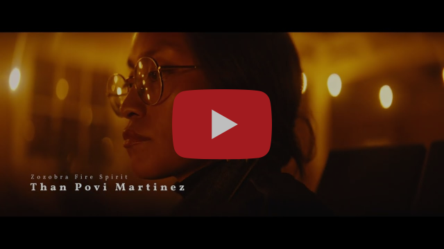A person with glasses stands in a softly lit room, text reads Zozobra Fire Spirit, Than Povi Martinez